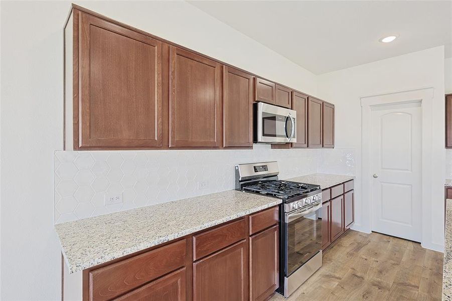 Kitchen with backsplash, light stone countertops, light hardwood / wood-style flooring, and appliances with stainless steel finishes