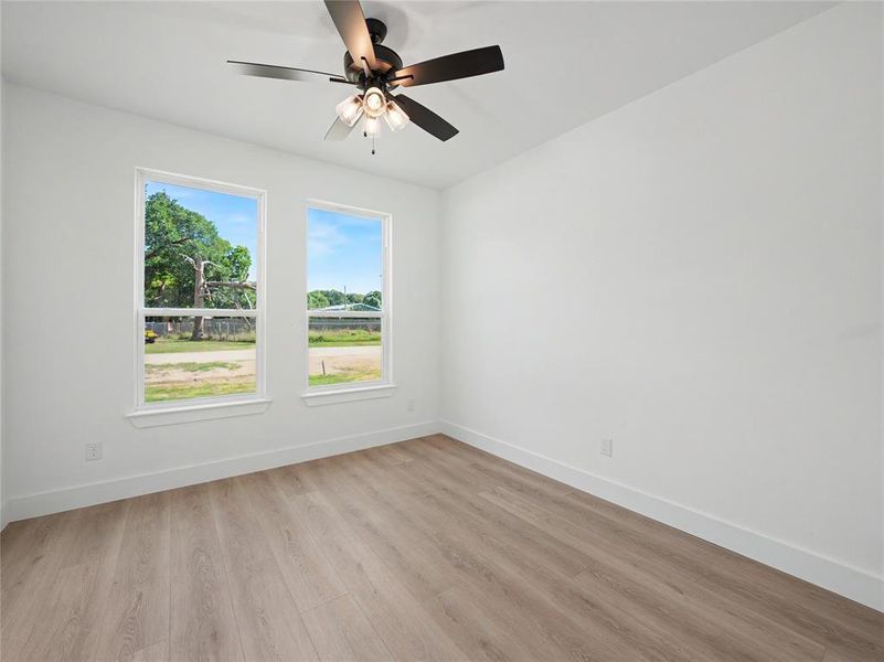 Room featuring wood-finish flooring, white baseboards, and two windows with white trim Room featuring wood-finish flooring, white baseboards, and two windows with white trim