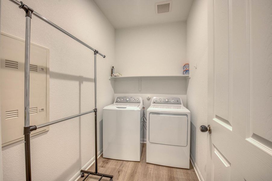 An organized laundry space features wood-style flooring and a built-in utility shelf.