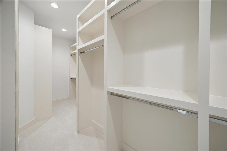 Expansive hanging rods and built-in shelving define the functionality of this primary closet. Open sections allow for easy organization of wardrobe items, while the clean design maintains a streamlined look. Neutral tones and recessed lighting enhance the overall sense of space and order.