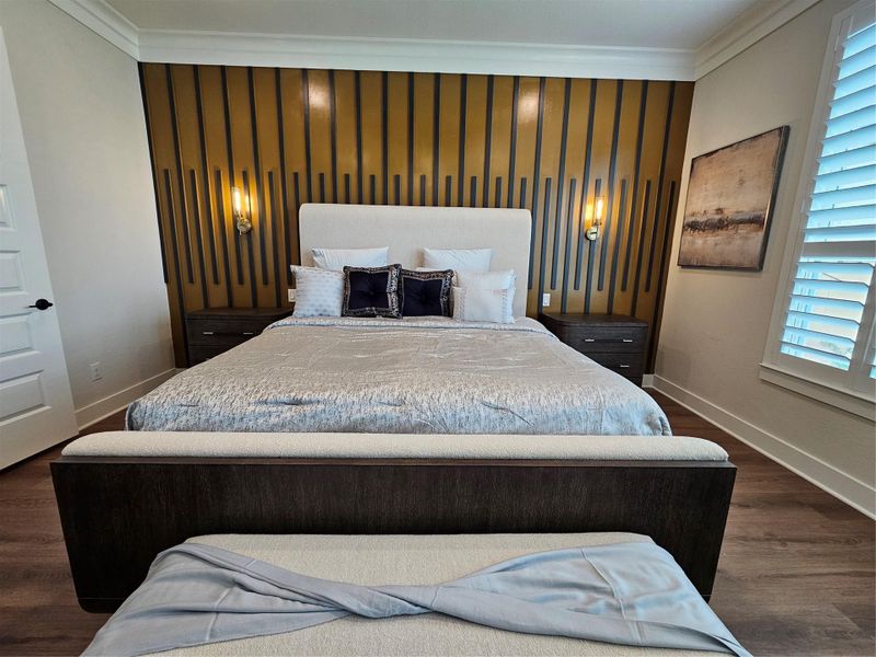 This bedroom features a stylish design with a modern accent wall, a large comfortable bed, and elegant bedside lighting. The room has hardwood flooring and a window with plantation shutters, providing ample natural light.
