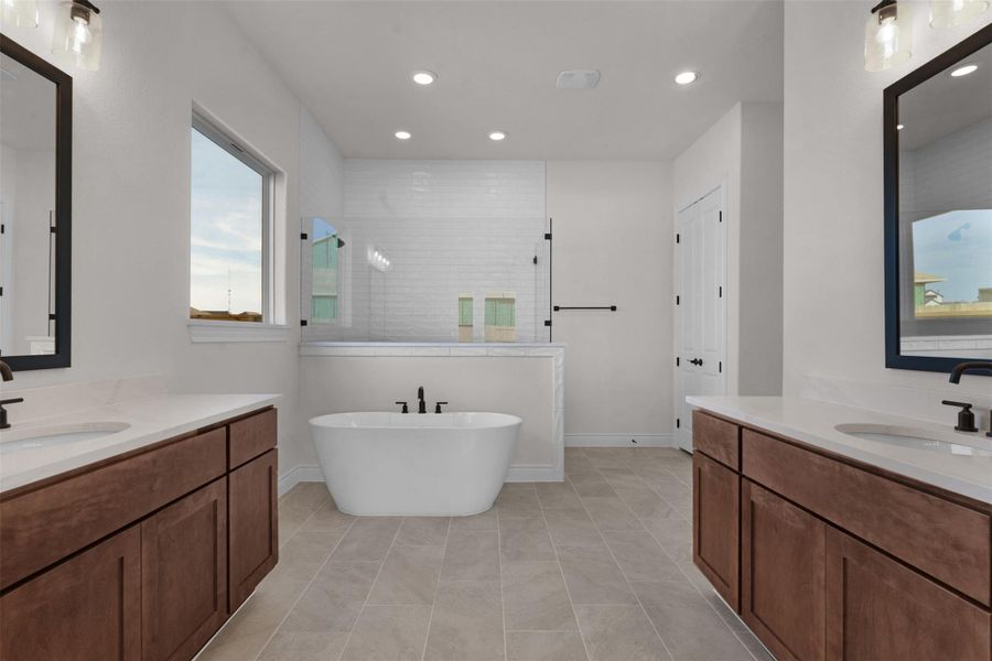 Bathroom featuring two vanities, walk in shower, a freestanding bath, recessed lighting, and light tile patterned flooring