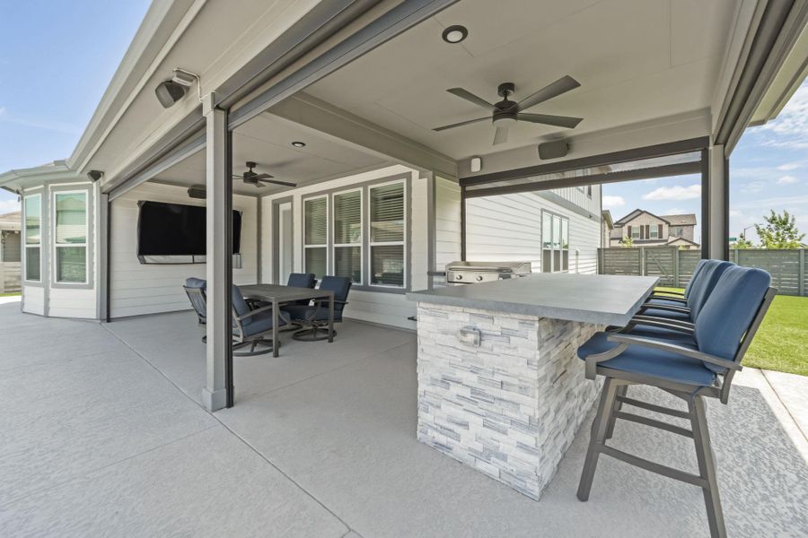 Outdoor living area featuring a built-in stone-finish island with integrated grill, ceiling fans, recessed lighting, and a dedicated television space