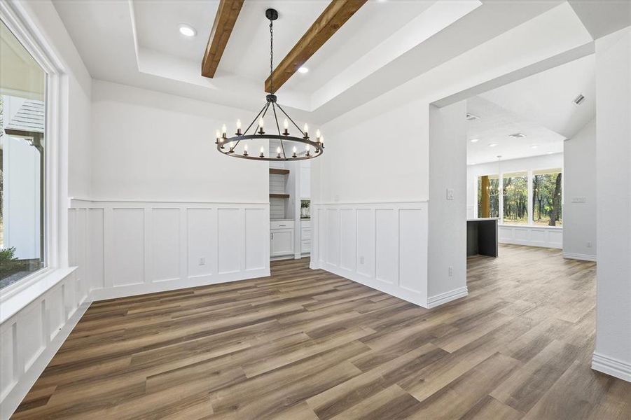 Unfurnished dining area featuring suspended lighting, beamed ceiling, a tray ceiling, wainscoting, and dark wood finished floors