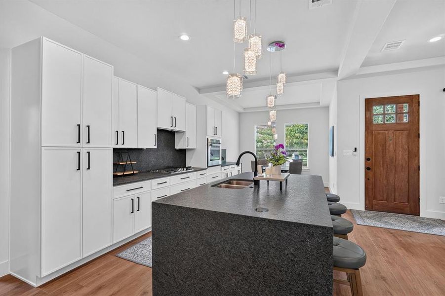 Spacious kitchen featuring an expansive dark stone island with integrated sink, white flat-panel cabinetry, a dark stone backsplash, and hardwood flooring