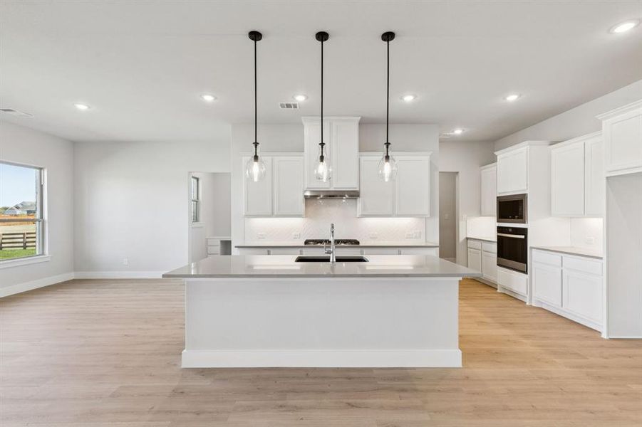 Kitchen with decorative backsplash, white cabinets, an island with sink, light wood finished floors, and recessed lighting
