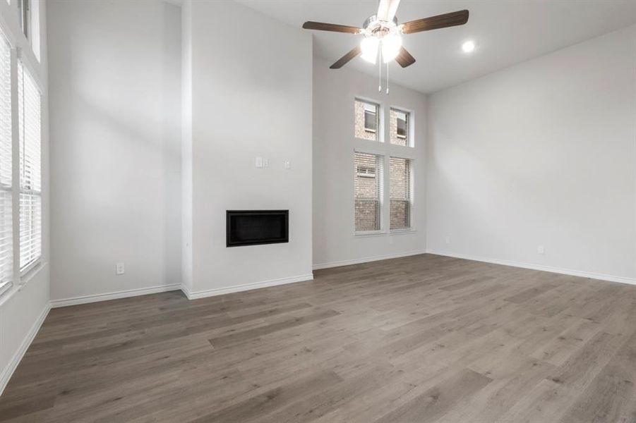 Unfurnished living room featuring a high ceiling, a ceiling fan, a fireplace, and dark wood-type flooring