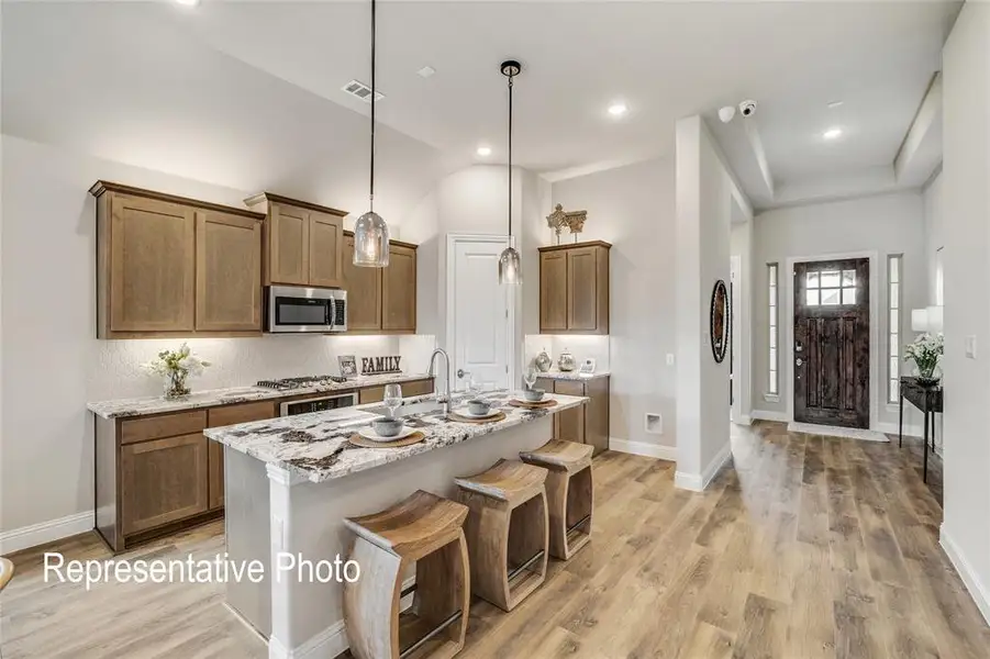 Kitchen featuring light stone counters, an island with sink, decorative light fixtures, light hardwood / wood-style flooring, and a kitchen breakfast bar