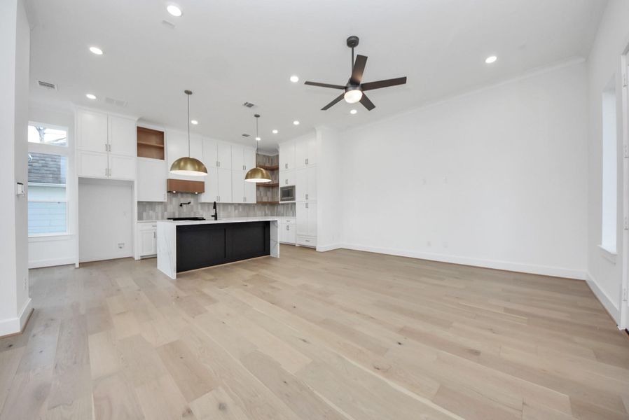A spacious open-concept living area designed for effortless everyday living and entertaining. The sleek kitchen offers white cabinetry, a large island, and modern pendant lighting, while light wood floors, recessed lighting, and a ceiling fan enhance the airy, inviting feel.