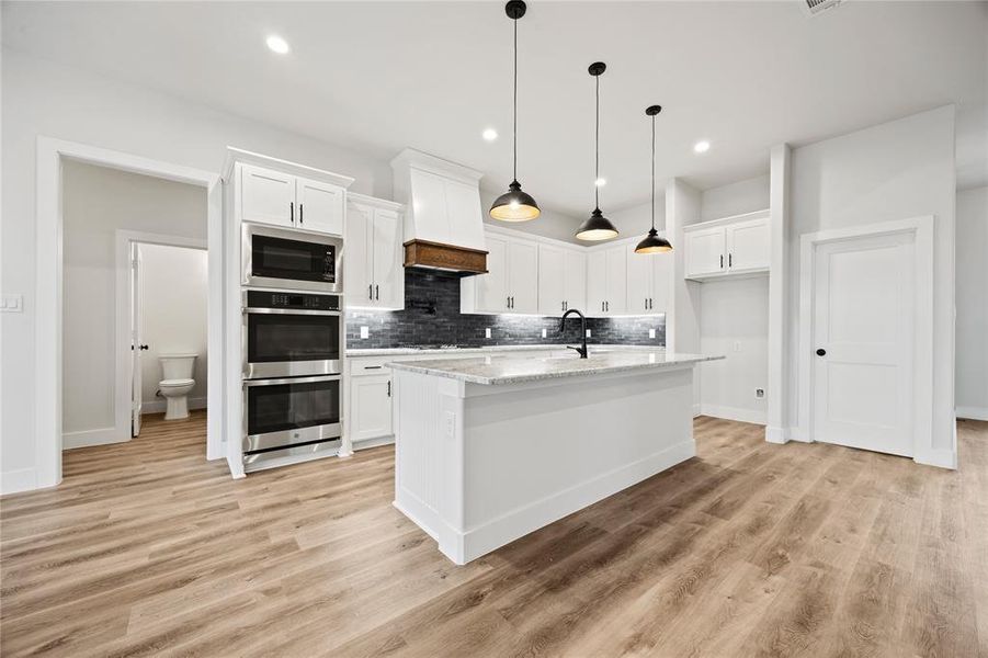 Kitchen with white cabinetry, stainless steel appliances, a center island with sink, and pendant lighting