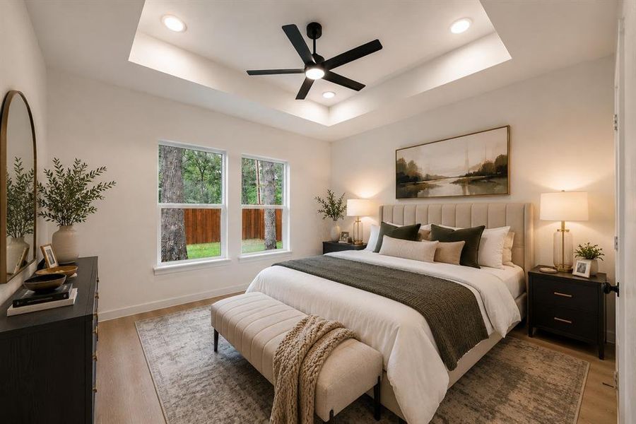 Spacious bedroom featuring light wood-finish flooring, a tray ceiling with recessed lighting, and a contemporary ceiling fan Spacious bedroom featuring light wood-finish flooring, a tray ceiling with recessed lighting, and a contemporary ceiling fan