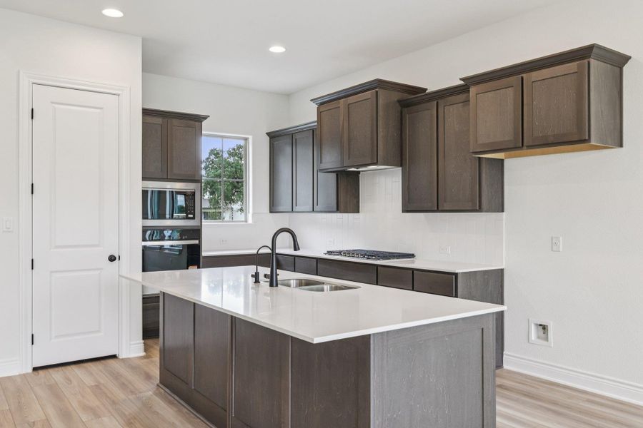 Kitchen with dark brown cabinetry, appliances with stainless steel finishes, light wood finished floors, recessed lighting, and a center island with sink