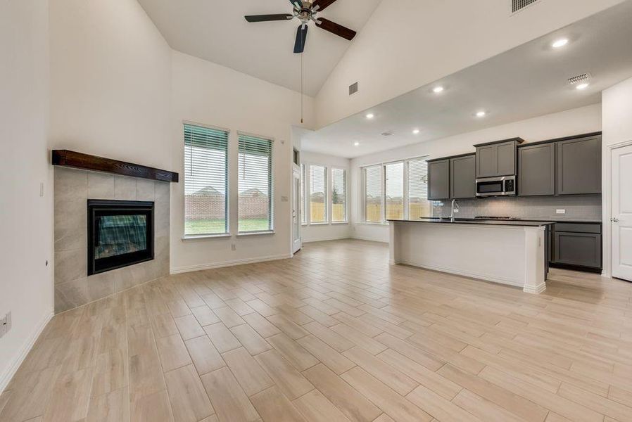 Kitchen with a kitchen island with sink, light hardwood / wood-style flooring, high vaulted ceiling, gray cabinets, and a fireplace