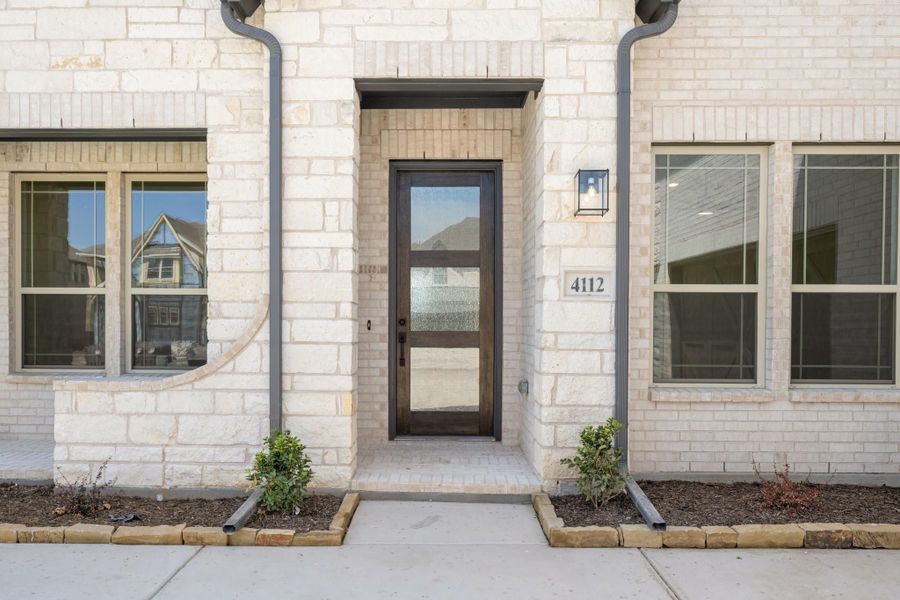 Front entry of home 4112 with dark wood glass-panel door, light brick exterior, and small landscaped beds on each side