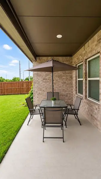 Covered patio with a smooth concrete surface, featuring brick siding, dual-pane windows, and a manicured lawn Covered patio with a smooth concrete surface, featuring brick siding, dual-pane windows, and a manicured lawn