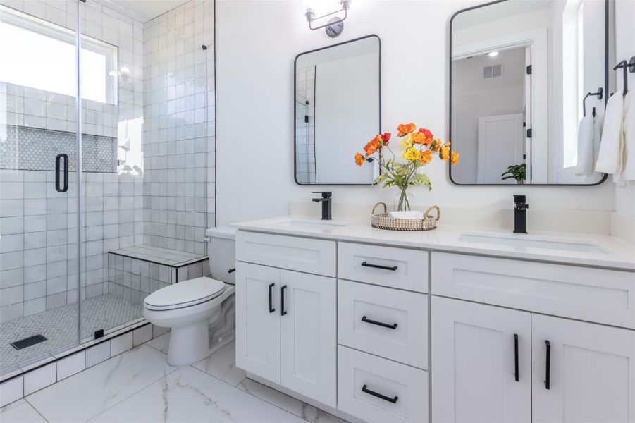 Full bath with a shower stall, double vanity, and light marble finish floors
