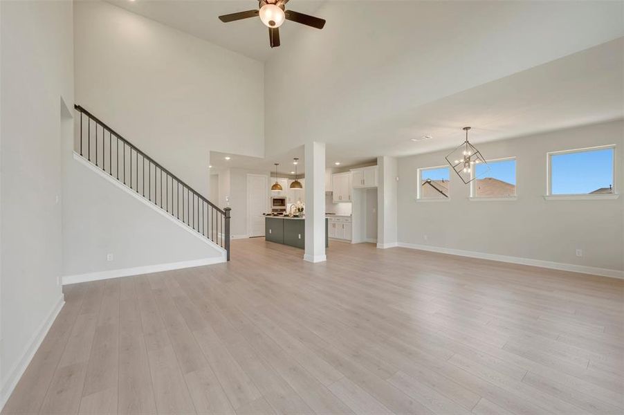 Spacious open-concept living area featuring light wood-finish flooring, a two-story ceiling, and a modern ceiling fan