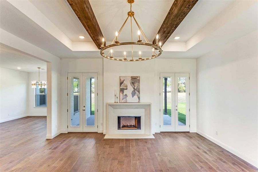 Unfurnished living room featuring french doors, a chandelier, beam ceiling, wood finished floors, and a fireplace Unfurnished living room featuring french doors, a chandelier, beam ceiling, wood finished floors, and a fireplace