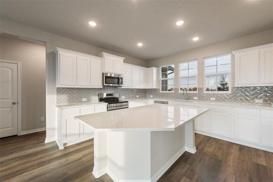 Kitchen featuring stainless steel appliances, white cabinetry, light stone countertops, dark wood-style floors, and a center island