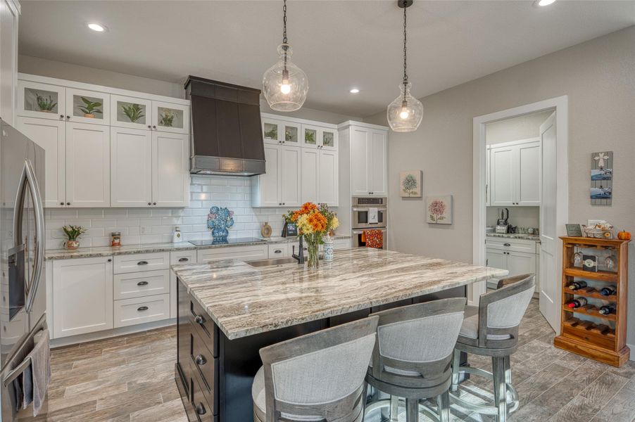 Kitchen with a kitchen bar, light stone counters, custom exhaust hood, tasteful backsplash, and white cabinets