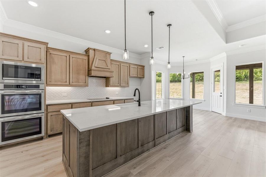 Kitchen featuring stainless steel appliances, a large island, crown molding, light wood-type flooring, and light stone counters