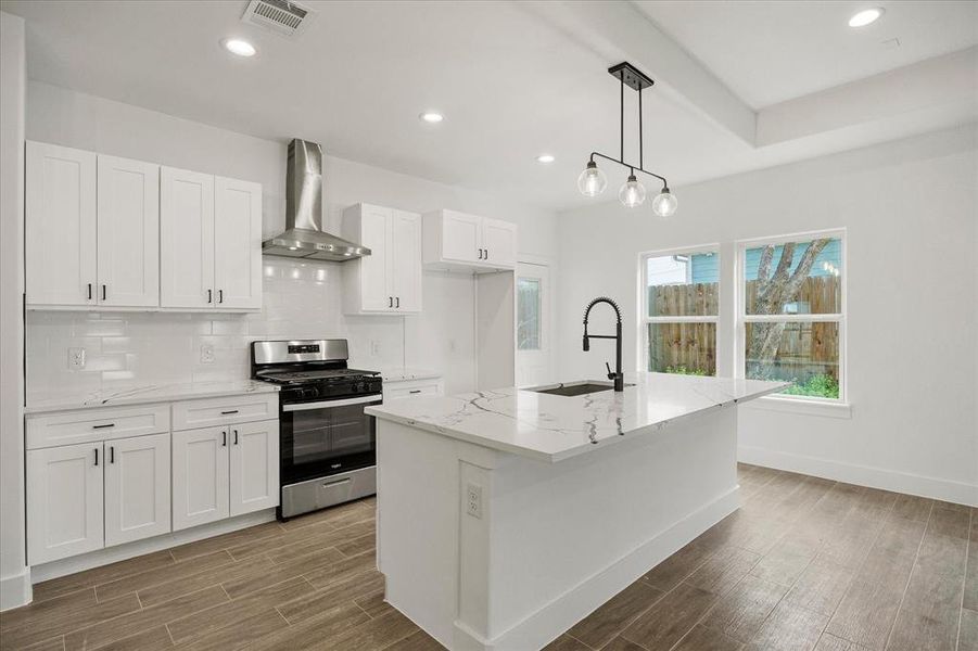 Kitchen with wood finish floors, gas stove, white cabinetry, light stone countertops, and backsplash