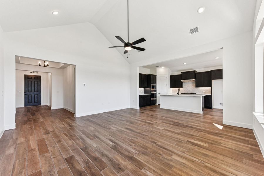 Unfurnished living room featuring high vaulted ceiling, ceiling fan, recessed lighting, dark wood finished floors, and a chandelier