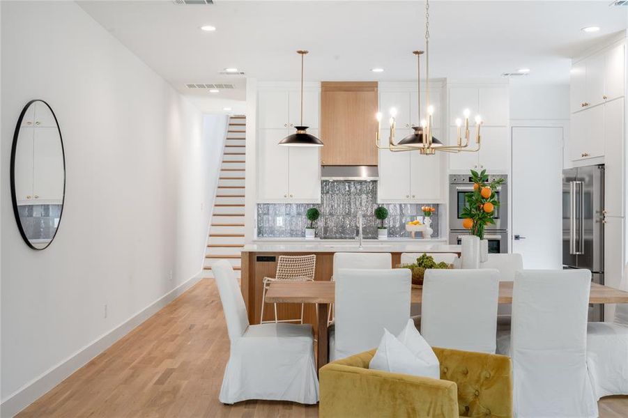 Kitchen with stainless steel appliances, light hardwood / wood-style floors, white cabinetry, decorative light fixtures, and range hood