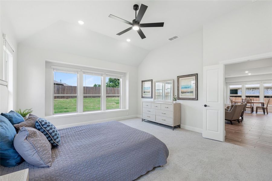 Spacious master bedroom with vaulted ceiling, ceiling fan, large windows, and carpet flooring Spacious master bedroom with vaulted ceiling, ceiling fan, large windows, and carpet flooring