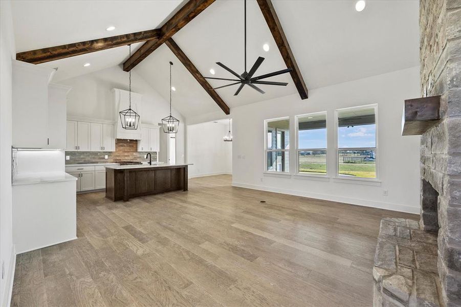 Kitchen with pendant lighting, a center island with sink, a stone fireplace, light wood-type flooring, and beamed ceiling