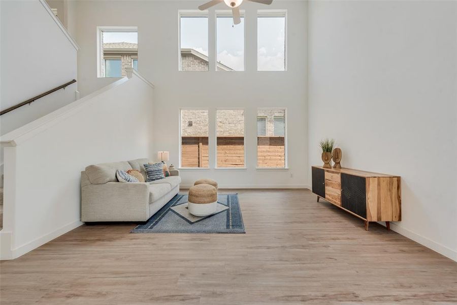 Living room with ceiling fan, a towering ceiling, and light wood-type flooring