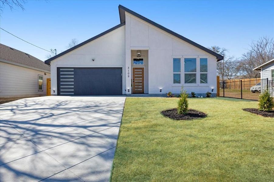 View of front of home with concrete driveway, an attached garage, fence, a front yard, and stucco siding