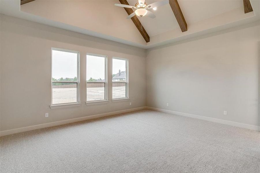 Carpeted empty room featuring lofted ceiling with beams and ceiling fan