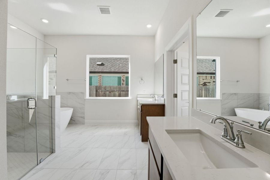 Bathroom with a soaking tub, a stall shower, two vanities, light marble finish flooring, and recessed lighting