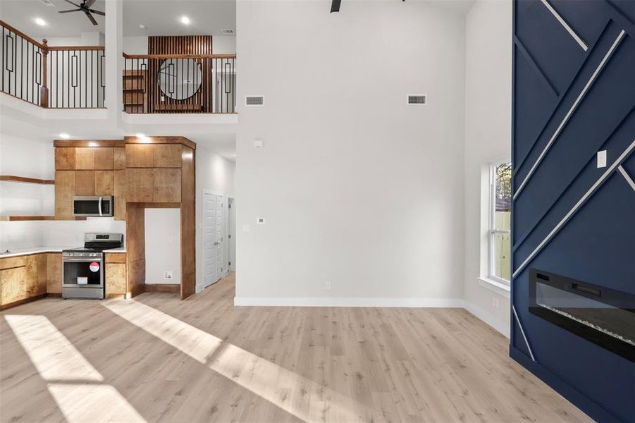 Kitchen featuring light wood-type flooring, appliances with stainless steel finishes, a towering ceiling, and ceiling fan