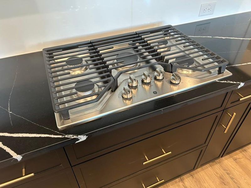 Kitchen view of stainless steel gas cooktop, light wood-type flooring, and dark cabinetry