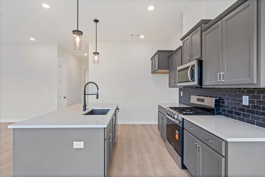 Kitchen featuring a central island with an integrated sink, pendant lighting, built-in stainless steel appliances, gray cabinetry, and white countertops