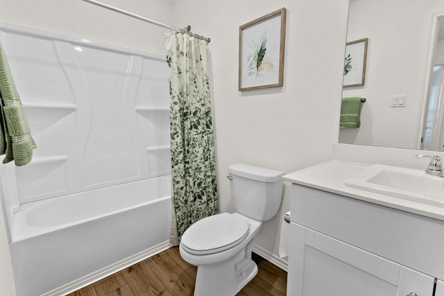 Bathroom featuring a white bathtub and shower surround, a white toilet, a vanity with a white countertop and integrated sink, chrome faucet, and wood-finish flooring