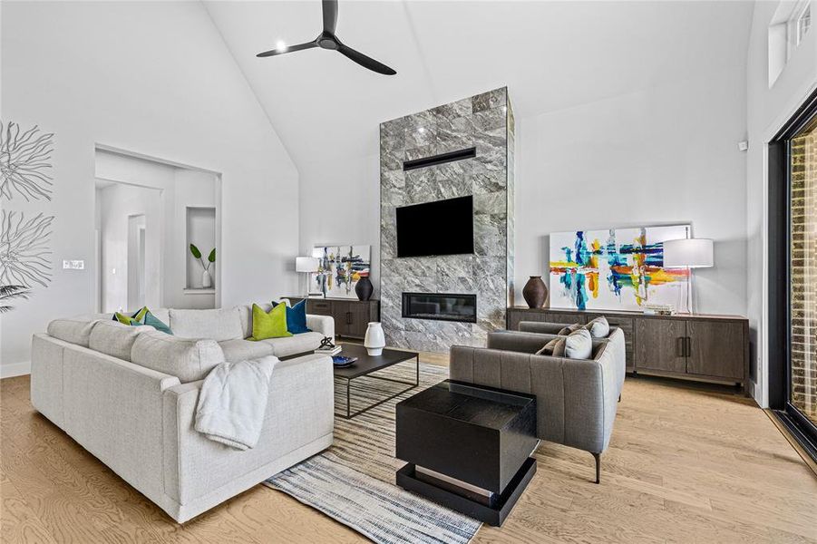 Living room featuring high vaulted ceiling, a glass covered fireplace, light wood-style floors, and a ceiling fan