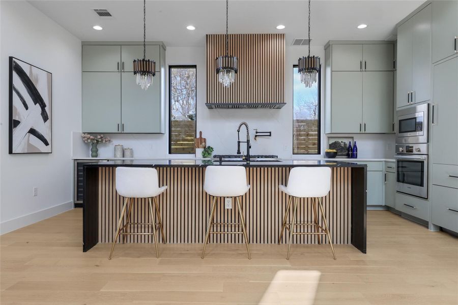 Kitchen with a kitchen island with sink, light wood-style flooring, a breakfast bar area, gray cabinetry, and stainless steel appliances