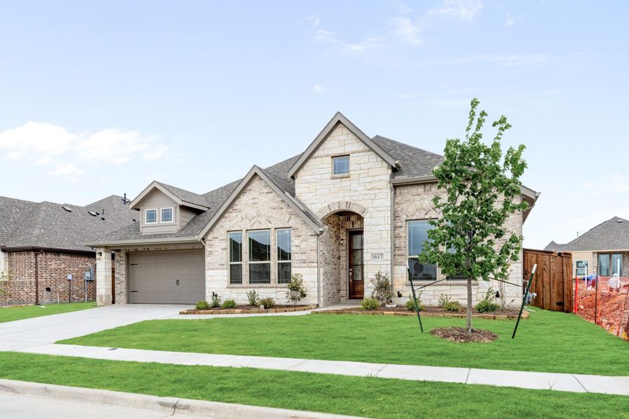 Single-story home with light stone exterior, arched entry, two-car garage, and manicured front lawn