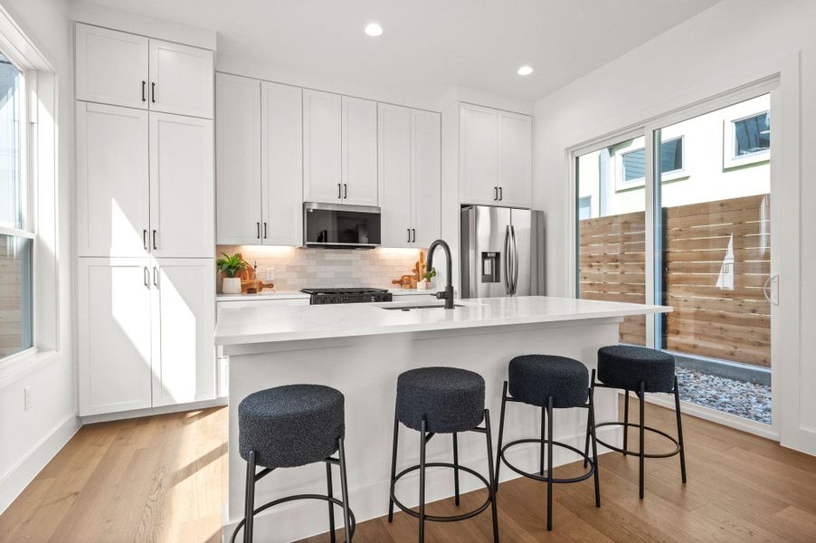 Kitchen with white cabinets, a center island with sink, a kitchen bar, light wood-style flooring, and recessed lighting