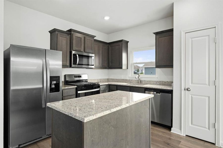 Kitchen with stainless steel appliances, dark brown cabinetry, light stone countertops, a center island, and dark wood-type flooring