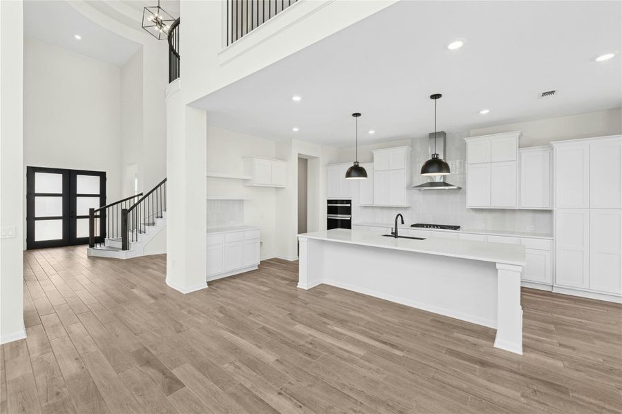Kitchen with french doors, white cabinets, pendant lighting, a center island with sink, and recessed lighting Kitchen with french doors, white cabinets, pendant lighting, a center island with sink, and recessed lighting