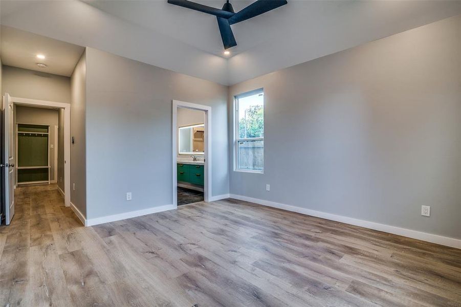 Unfurnished bedroom with ensuite bathroom, ceiling fan, and light hardwood / wood-style floors