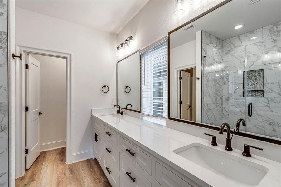 Full bath with a marble finish shower, visible vents, a sink, and wood finished floors Full bath with a marble finish shower, visible vents, a sink, and wood finished floors