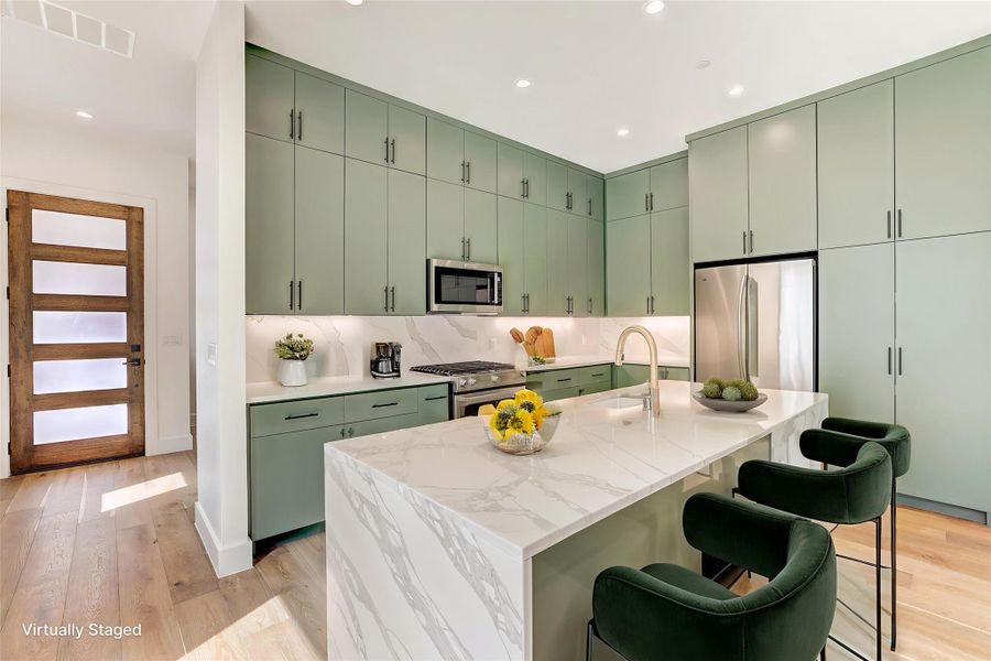 Kitchen featuring green cabinets, appliances with stainless steel finishes, recessed lighting, a breakfast bar area, and light wood finished floors