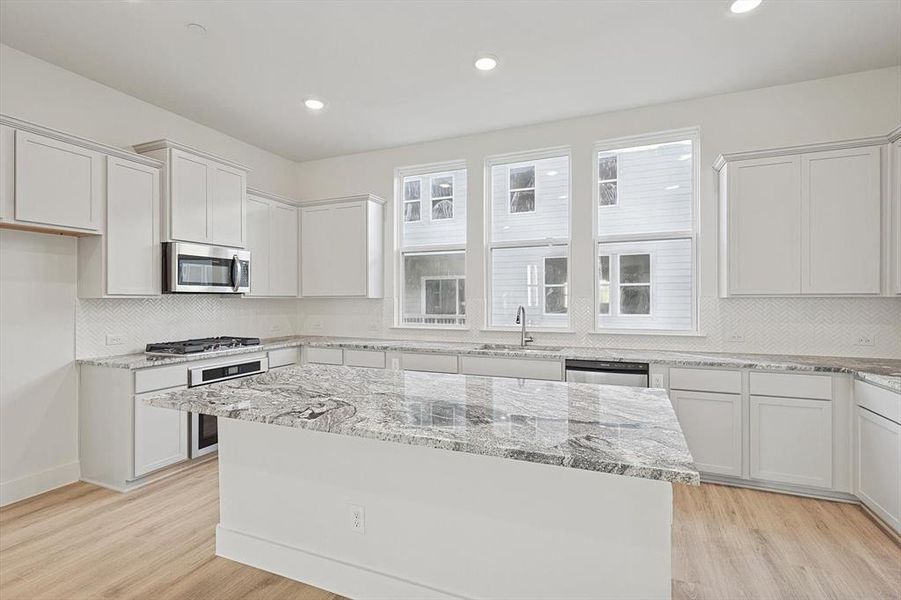 Kitchen with light wood-style flooring, a center island, appliances with stainless steel finishes, and a sink