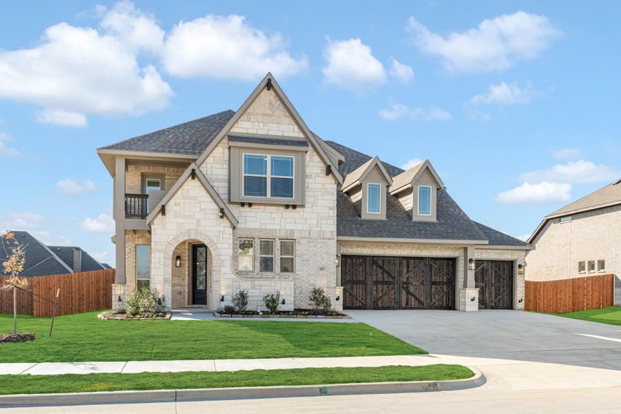 Two-story stone home with arched entry, three-car garage with wood doors, and manicured front lawn