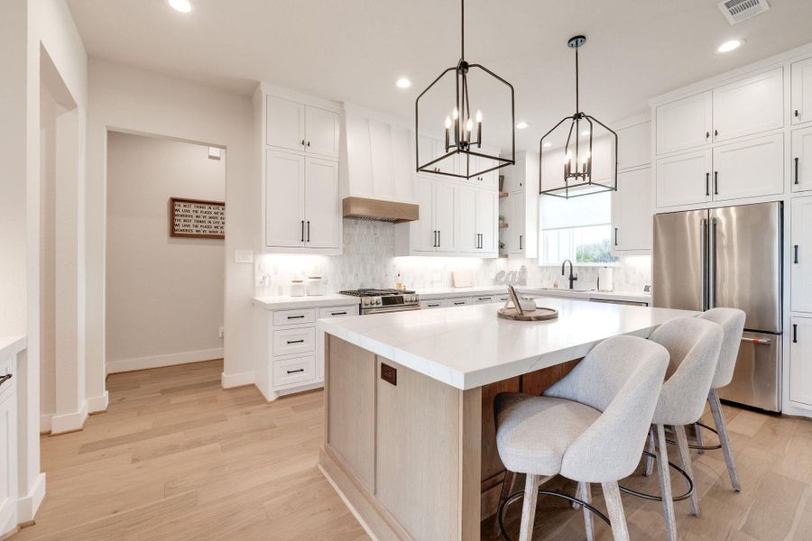 Kitchen featuring premium appliances, decorative backsplash, a chandelier, light wood-style floors, and two tone cabinets